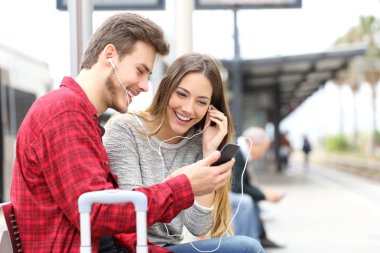 Mutlu yolcuları bir akıllı telefon ve kulaklık ile müzik paylaşımı bir tren istasyonunda bekleyen birkaç