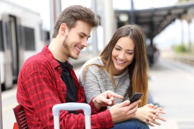 Bir tren istasyonunda bekleyen bir akıllı telefon ile online otel rezervasyon iki mutlu gezginler
