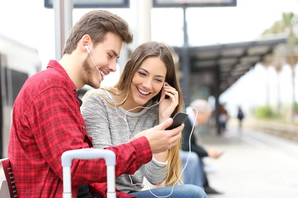 Dva Šťastné Cestující Čekající Nádraží Sdílení Hudby Chytrý Telefon Sluchátka — Stock fotografie