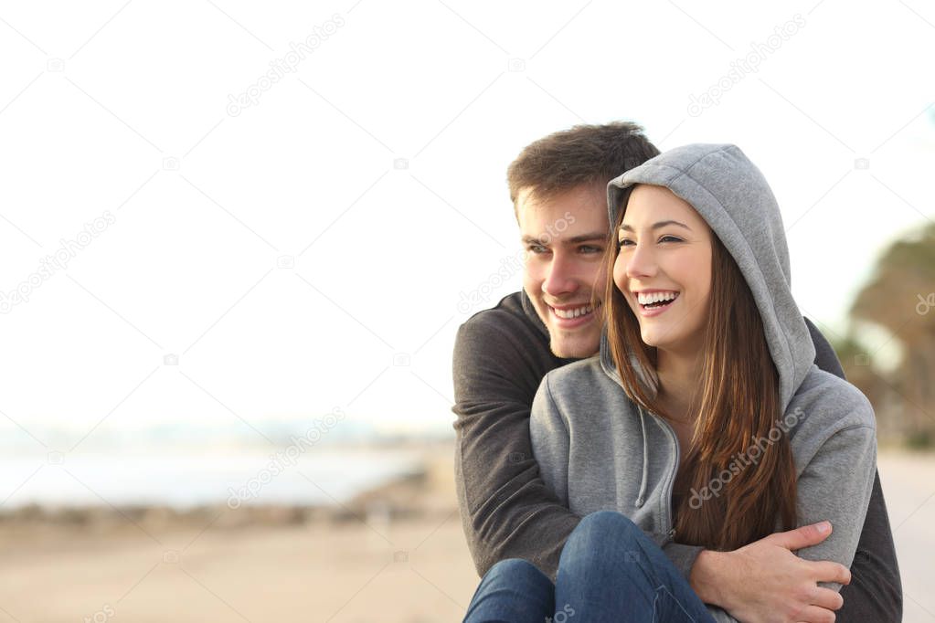 Couple of happy teens looking away and laughing on the beach