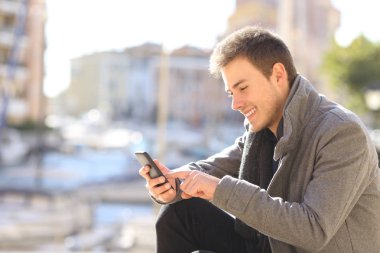 Yan görünümü bir akıllı telefon kışın bir sahil kasabasında sokak kullanarak mutlu bir adam portresi