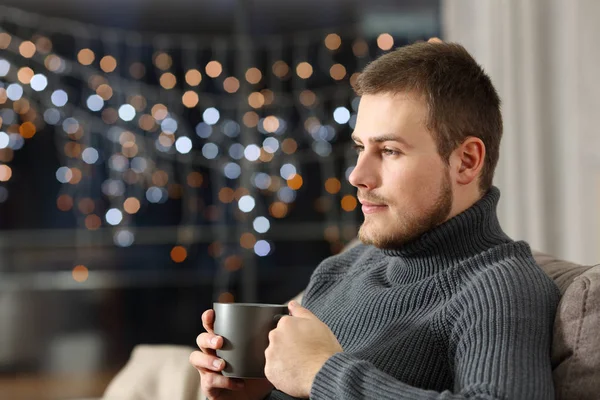 自宅のリビング ルームでソファの上に座っている夜にコーヒー カップを保持して物思いにふける男 — ストック写真
