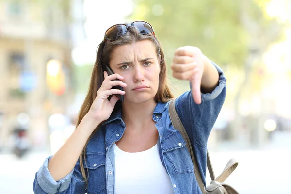 前视图肖像一个愤怒的女孩在电话中用拇指在街上说话 — 图库照片