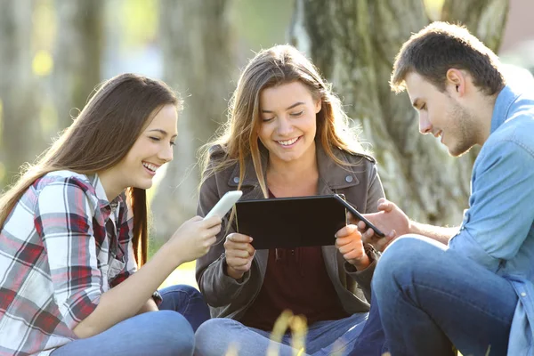 Tre Amici Felici Che Usano Più Dispositivi Seduti Sull Erba — Foto Stock