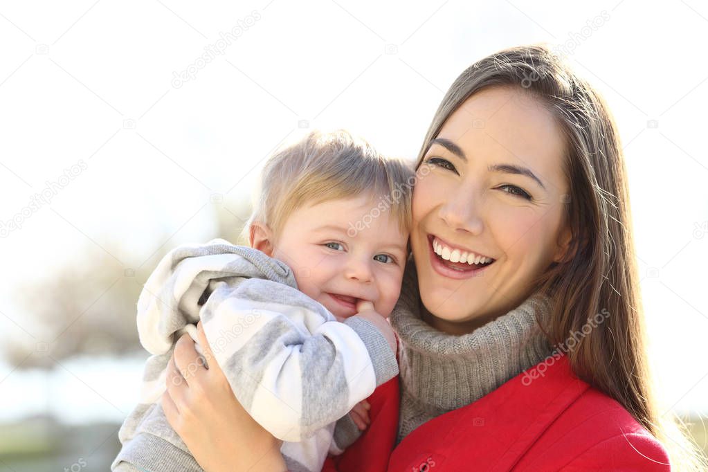 Front view portrait of a happy mother holding her son baby looking at you outdoors in winter