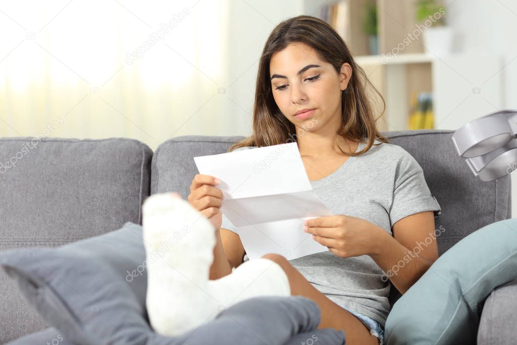 Relaxed disabled woman reading a letter sitting on a couch in the living room at home