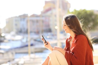 Bir akıllı telefon bir sahil kasabasında tatile kullanarak mutlu bir kadın profili