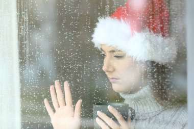 Üzgün ve yalnız kadın cam, yağmurlu bir gün Noel zamanında el ile dokunmak bir pencereden arıyor