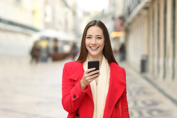 冬の路上で携帯電話を保持しているカメラを見ると赤い幸せな女 — ストック写真