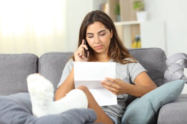 Disabled woman calling on phone about a letter sitting on a couch in the living room at home clipart