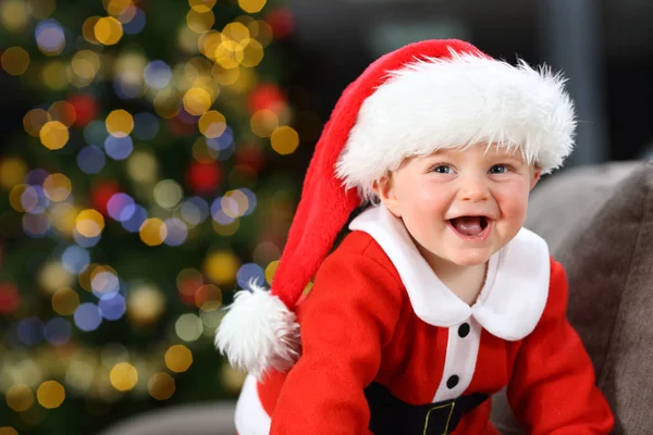 背景の木とクリスマスの自宅のソファの上身に着けているサンタ クロースの変装を笑って赤ちゃん — ストック写真