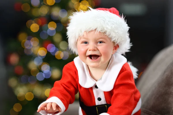 快乐的婴儿穿着圣诞老人服装在家里的沙发上 在圣诞节与一棵树的背景 — 图库照片