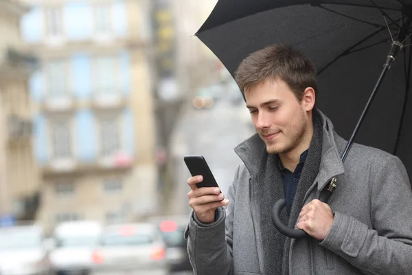 Człowiek Sprawdzanie Zawartości Inteligentny Telefon Trzymając Parasol Zimowy Deszczowy Dzień — Zdjęcie stockowe