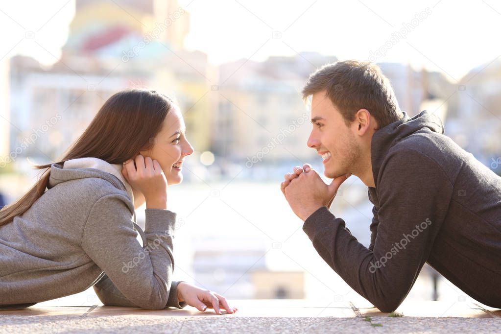 Side view portrait of a couple of teens in love looking each other in a coast town