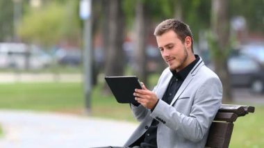 Bir tablet ve bir parkta bir bankta oturmuş şikayet kötü online haber işadamı okur