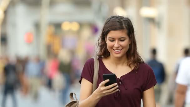 一个快乐的女人走向相机和使用智能手机在街上的前视图 — 图库视频影像