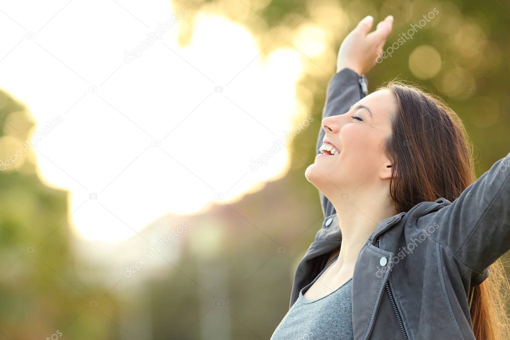 Side view portrait of a happy lady breathing fresh air raising arms in a park