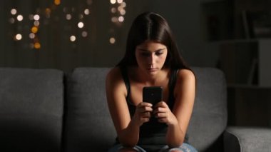 Siber zorbalık gece evde bir kanepede oturan telefon mesajı okuma üzgün bir kız önden görünümü