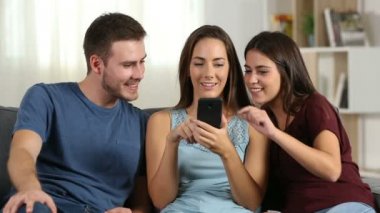 Evde akıllı telefon içeriği hakkında konuşan üç mutlu arkadaşlar önden görünümü bir kanepede oturan