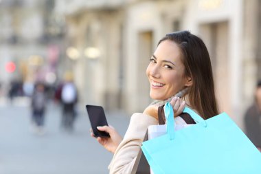 Mutlu müşteri bir akıllı telefon ve boş alışveriş torbaları sokakta yürürken holding