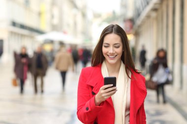 Kırmızı kış aylarında sokakta bir cep telefonu kullanarak kameraya doğru yürüyüş mutlu kadın