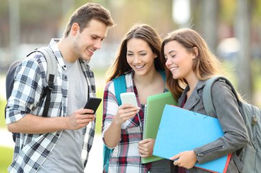 Medya içeriklerinde akıllı telefonlarını bir parkta izlerken üç mutlu öğrenciler