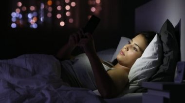 Ciddi kız gece evde yatakta yatan bir akıllı telefon sohbet