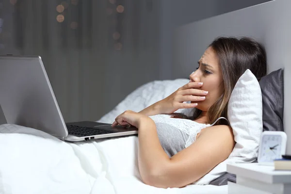 担心的妇女发现坏消息在一台笔记本电脑在床上晚上在家 — 图库照片