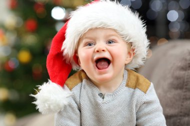 Neşeli bebek evde oturma odasında kanepede bir ağaç arka planda Noel kameraya bakıyor