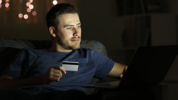 オンライン クレジット カードと夜自宅のソファに座ってノート パソコンを払って幸せな男 — ストック動画