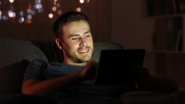 Medya bir tablet ile oturma odasında evde bir kanepede oturan gece izleyen adamım