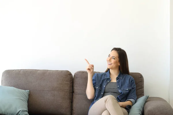 Wanita Duduk Sofa Menunjuk Dinding Putih Terisolasi — Stok Foto