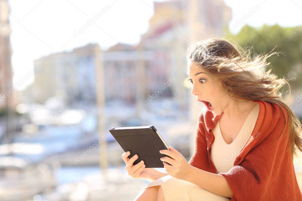 Shocked woman watching online content in a tablet in a coast town
