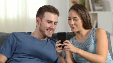 Oturma odasında evde bir kanepede oturan akıllı telefon içeriği hakkında konuşmak mutlu çift
