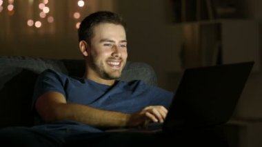 Mutlu adam gece oturma odasında evde bir kanepede oturan bir laptop yazma