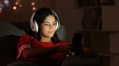 Mutlu bir kanepede oturan genç şarkı seçerek ve akıllı ve kulaklık ile müzik şarkı telefon