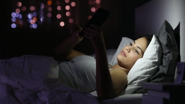 夜に自宅のベッドでスマート フォンでオンラインの良いニュースを読んで興奮している女の子 — ストック動画