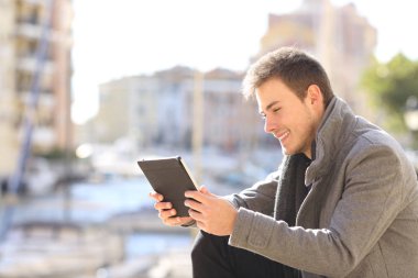 Yan görünümü mutlu bir adam portresi bir tablet dışında bir sahil kasabası sokakta kullanır.