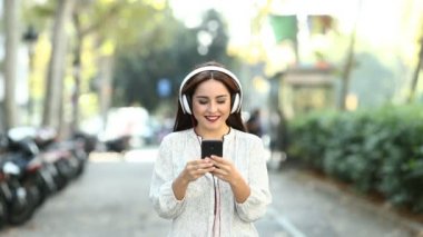 Ağır çekimde bir akıllı telefon ile müzik dinlerken kameraya doğru yürüyen bir mutlu kadın önden görünüm kaydedildi