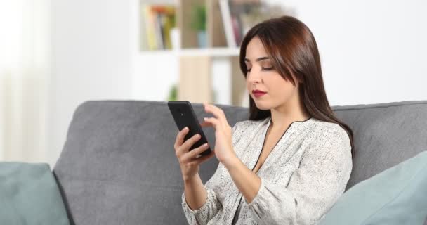 Seriózní žena procházení obsahu v chytrý telefon na gauči v obývacím pokoji doma