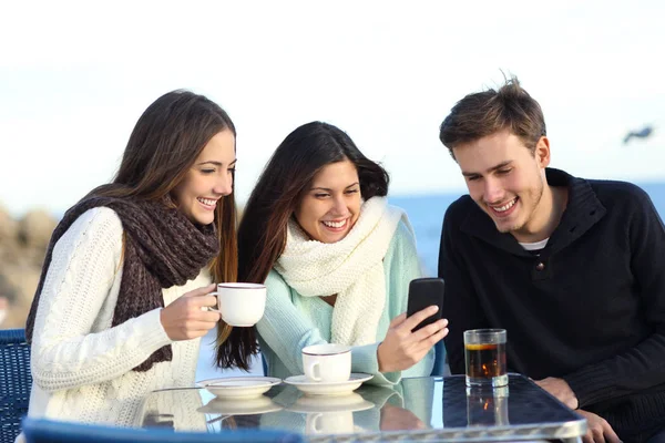 Three Happy Friends Watching Media Content Smart Phone Bar Winter Stock Image