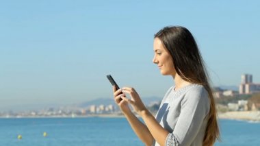 Sahilde online teklif bulma bir akıllı telefon kullanan heyecanlı bir kadın profili. Ağır çekim
