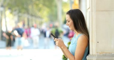 Mutlu kadın manifatura sokakta bir duvara yaslanmış bir akıllı telefon üzerinde profili