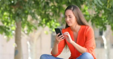 Şok kadın finging online teklifi bir parkta bir bankta oturmuş bir akıllı telefon