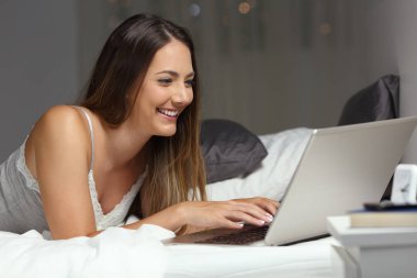 Mutlu kadın gece evde bir yatakta yatarken bir dizüstü bilgisayarda yazarak