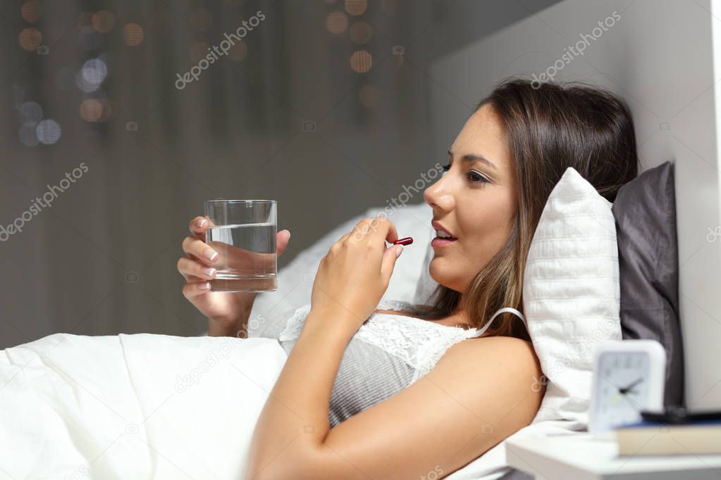 Profile of a happy girl taking a pill before sleep on a bed in the night at home