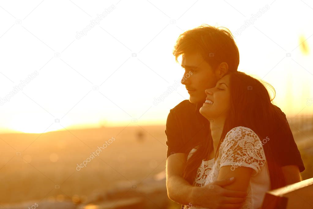 Happy couple in love dating and flirting at sunset sitting on a bench on the beach