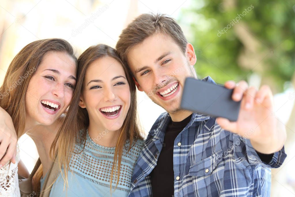 Portrait of three happy friends taking selfies together with a smart phone in the street