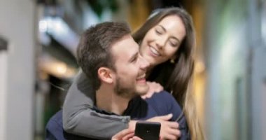 Mutlu bir çift sokakta gece izlerken akıllı telefon içerik şaka kameraya doğru yürüyüş önden görünümü