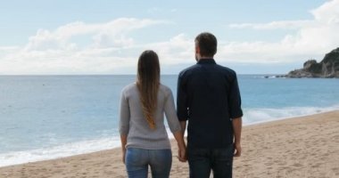 Mutlu bir çift holding yürüyüş arkadan görünüm Sahilde güneşli bir günde eller.
